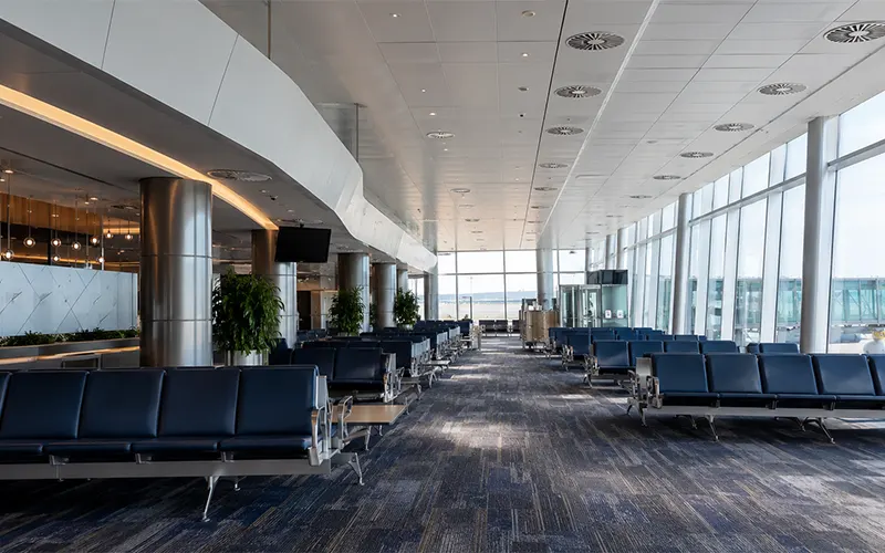 Área de espera de aeropuerto con difusores HVAC en el techo, asientos para pasajeros y distribución de aire interior.