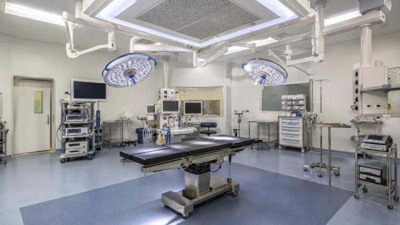 Quirófano hospitalario moderno con mesa de operaciones, lámparas quirúrgicas y sistema de ventilación en el techo para el control del aire.